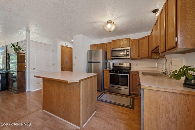 kitchen featuring a textured ceiling, a center island, stainless steel appliances, light hardwood / wood-style floors, and sink