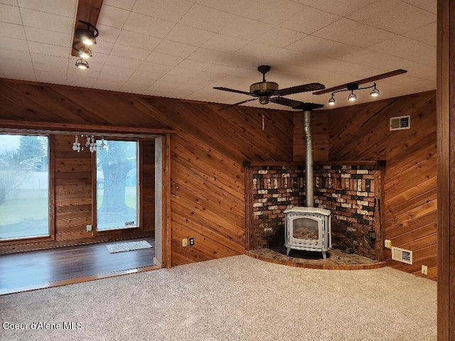 unfurnished living room with track lighting, wood walls, ceiling fan, and a wood stove