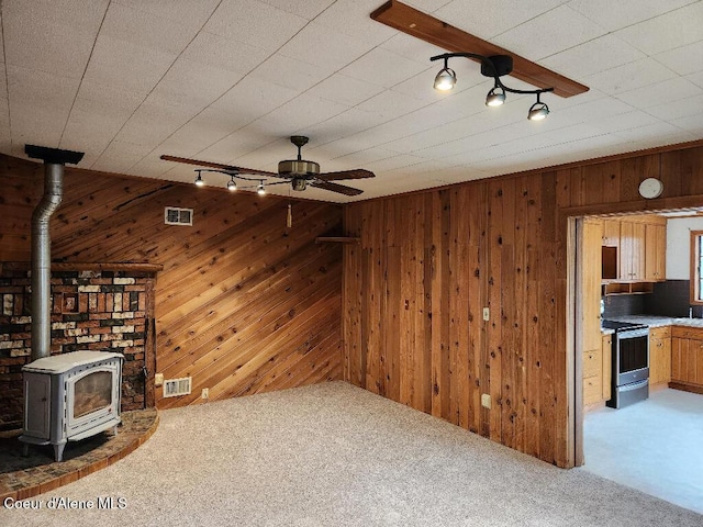 unfurnished living room with wood walls, a wood stove, and light carpet