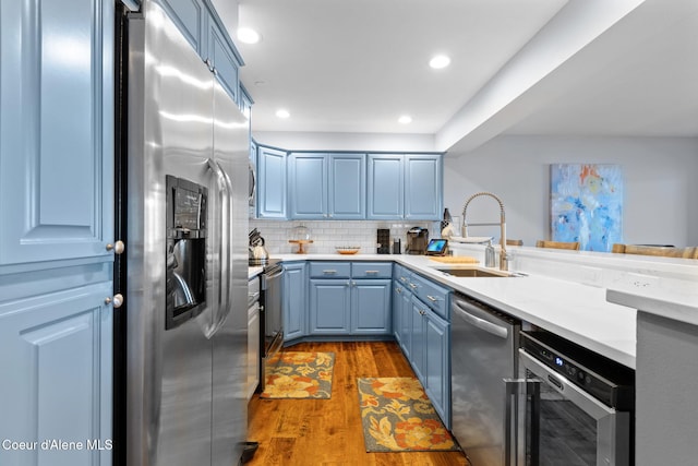 kitchen with sink, blue cabinets, light wood-type flooring, and appliances with stainless steel finishes