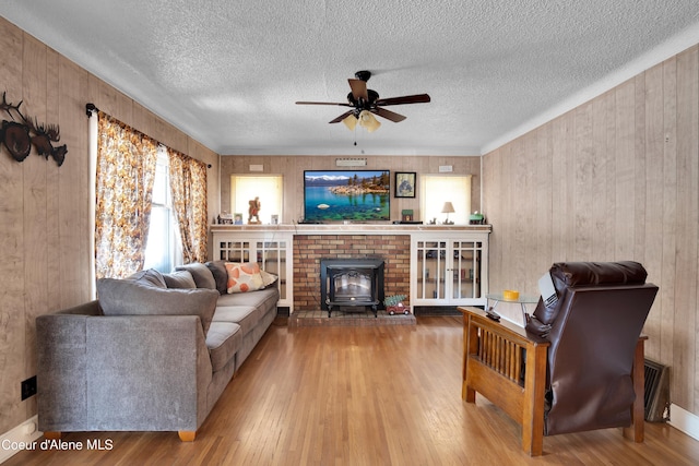 living room featuring a wood stove, ceiling fan, wooden walls, and hardwood / wood-style floors