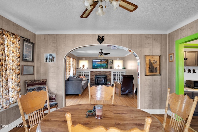 dining room with light hardwood / wood-style flooring, ceiling fan, a textured ceiling, ornamental molding, and wooden walls