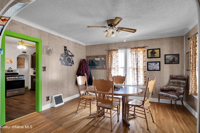 dining space featuring ceiling fan, dark wood-type flooring, a textured ceiling, and wooden walls