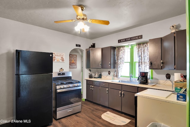 kitchen featuring sink, dark brown cabinets, black fridge, dark hardwood / wood-style floors, and stainless steel range with gas cooktop