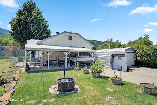 back of property featuring a garage, a patio area, a yard, and an outbuilding