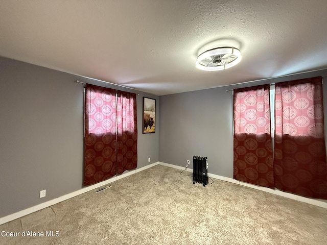 empty room featuring radiator, a textured ceiling, and carpet