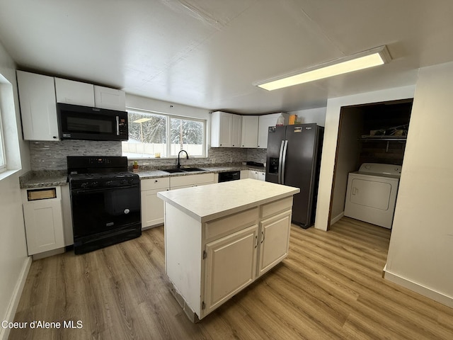 kitchen with black appliances, a kitchen island, white cabinetry, washer / clothes dryer, and sink