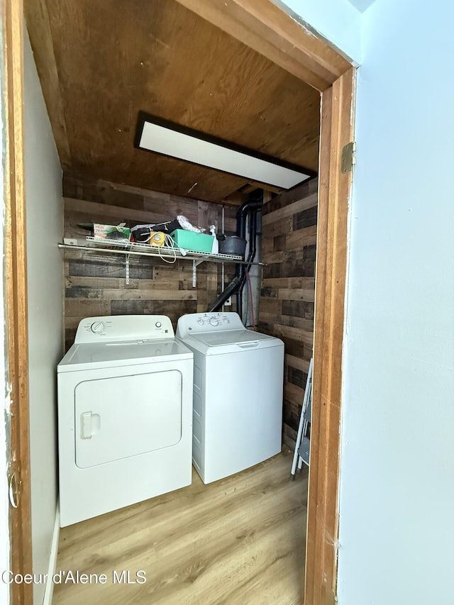 laundry room with wooden walls, washer and clothes dryer, and light wood-type flooring