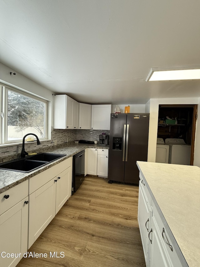 kitchen with dishwasher, stainless steel refrigerator with ice dispenser, white cabinets, washing machine and clothes dryer, and sink