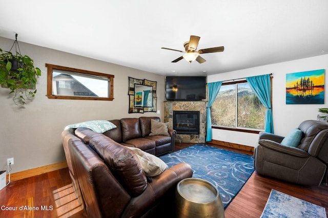 living room with dark wood-type flooring, a stone fireplace, and ceiling fan