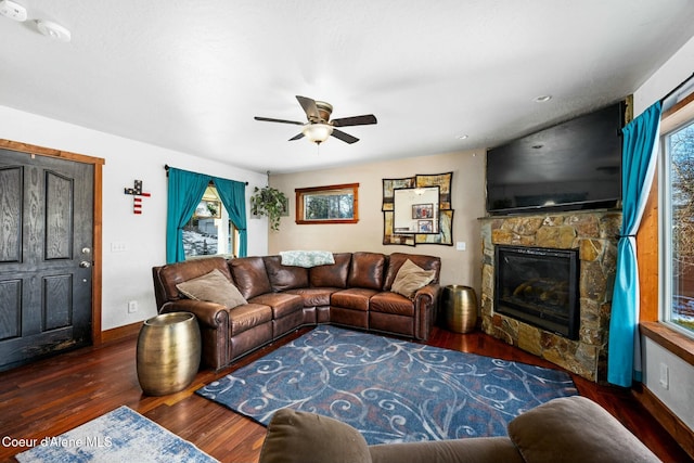 living room featuring ceiling fan, dark wood-type flooring, and a stone fireplace