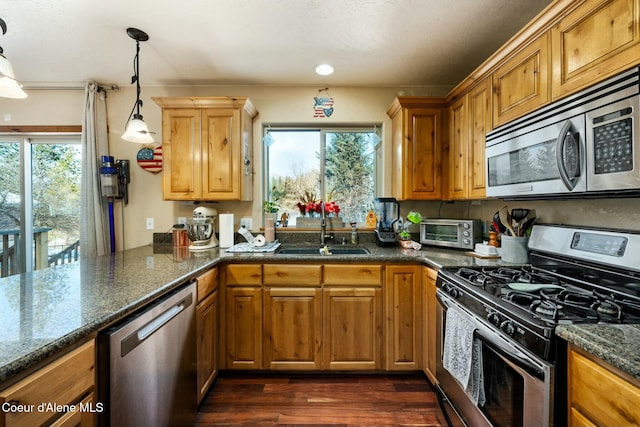 kitchen featuring stainless steel appliances, dark stone countertops, decorative light fixtures, and sink