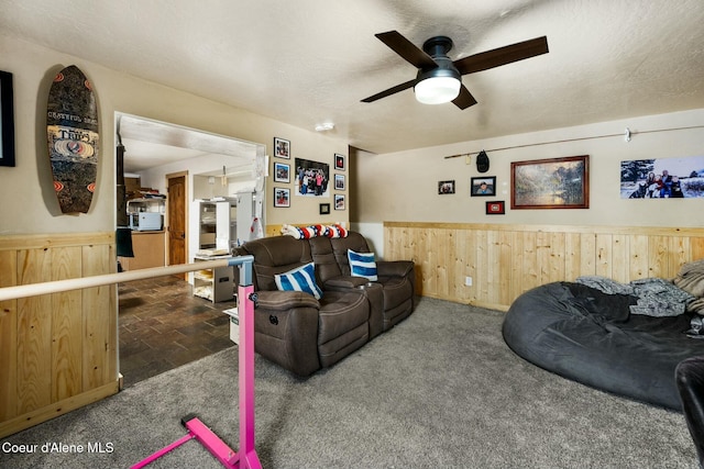 carpeted living room featuring ceiling fan, wood walls, and a textured ceiling