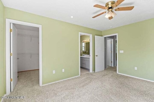 unfurnished bedroom featuring ceiling fan, a spacious closet, connected bathroom, light carpet, and a closet