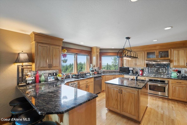 kitchen with pendant lighting, appliances with stainless steel finishes, exhaust hood, a center island with sink, and a breakfast bar area