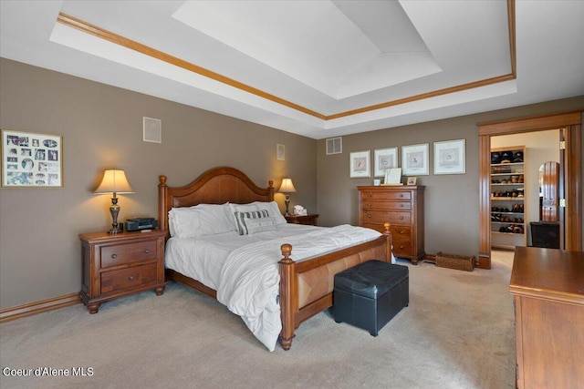 bedroom featuring a spacious closet, light colored carpet, and a raised ceiling