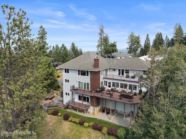 rear view of house featuring a lawn, a patio area, a wooden deck, and a balcony