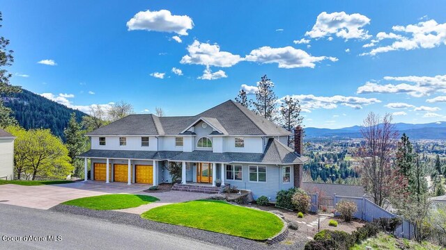view of front of home with concrete driveway, a chimney, a mountain view, fence, and a front yard
