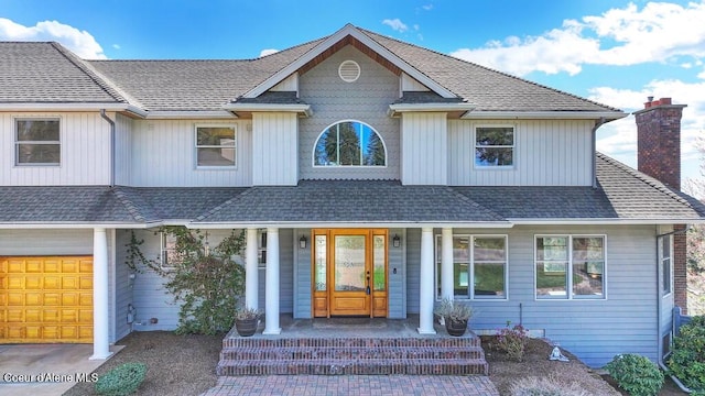 view of front of house featuring a chimney, a shingled roof, and covered porch