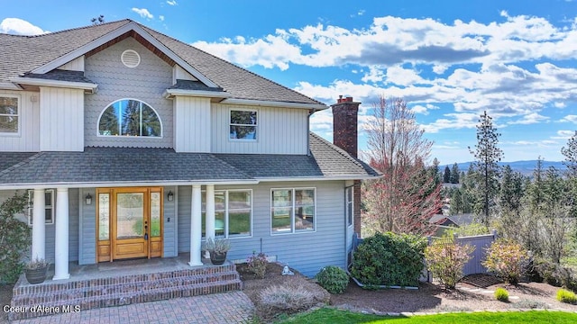 view of front of home with a shingled roof, a chimney, and covered porch
