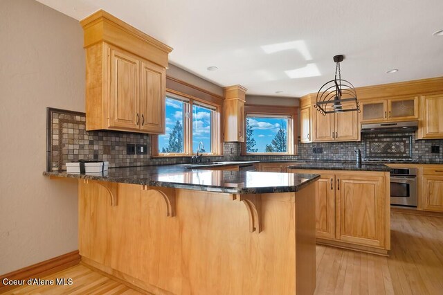 kitchen with light wood-type flooring, a peninsula, under cabinet range hood, and a kitchen bar