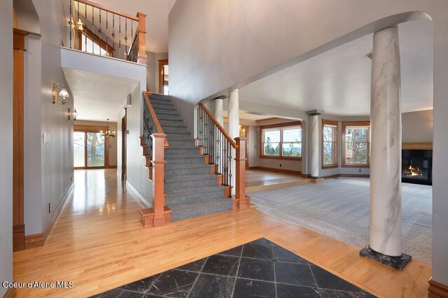 stairway with a glass covered fireplace, a towering ceiling, baseboards, and decorative columns