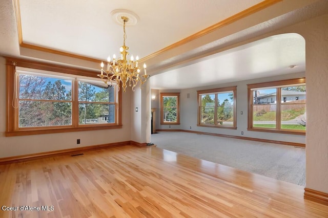 unfurnished room featuring wood finished floors, a chandelier, arched walkways, a raised ceiling, and baseboards