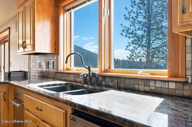 kitchen with brown cabinets, tasteful backsplash, dark stone counters, and a sink