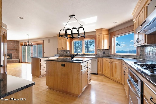 kitchen featuring range hood, a sink, a center island, a chandelier, and appliances with stainless steel finishes