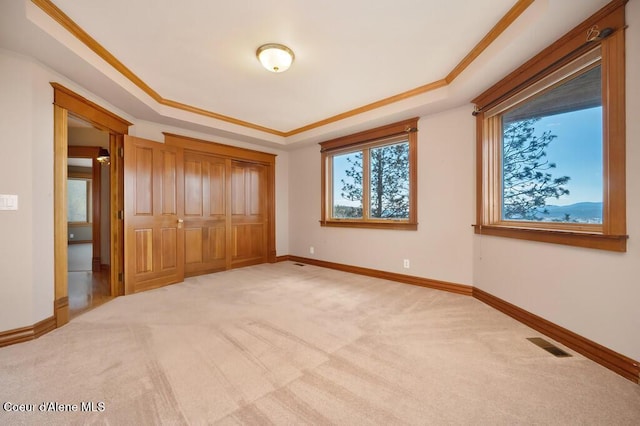 unfurnished bedroom featuring light carpet, a tray ceiling, visible vents, baseboards, and a closet