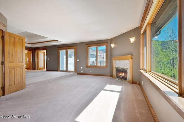 unfurnished living room featuring a fireplace with flush hearth, light carpet, baseboards, and a tray ceiling