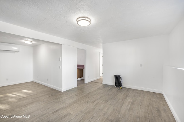 empty room with radiator, a textured ceiling, light hardwood / wood-style flooring, and a wall mounted air conditioner