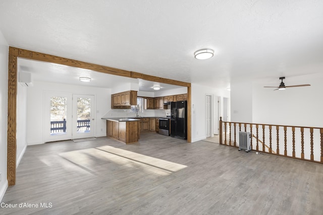 kitchen featuring stainless steel electric range oven, light hardwood / wood-style floors, ceiling fan, black fridge, and radiator heating unit