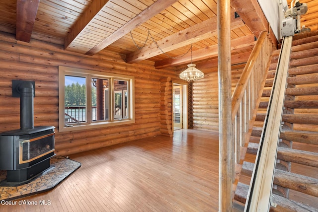 unfurnished living room with beamed ceiling, rustic walls, a notable chandelier, and a wood stove