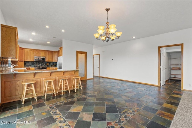 kitchen featuring stainless steel appliances, an inviting chandelier, backsplash, kitchen peninsula, and a breakfast bar area