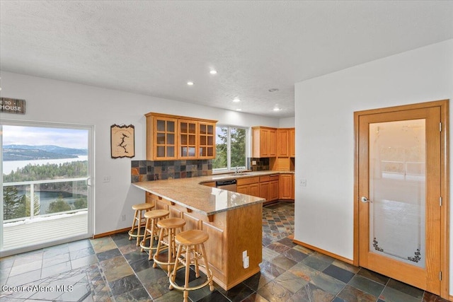 kitchen with a kitchen breakfast bar, kitchen peninsula, dishwasher, sink, and decorative backsplash