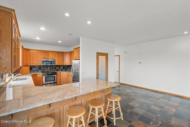 kitchen featuring light stone countertops, appliances with stainless steel finishes, tasteful backsplash, kitchen peninsula, and a breakfast bar