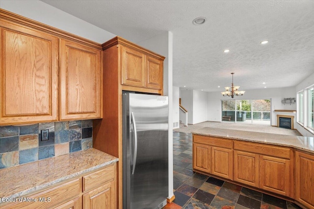 kitchen with light stone counters, a textured ceiling, and stainless steel refrigerator