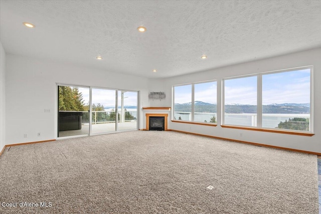 unfurnished living room with a textured ceiling, a water view, and carpet floors