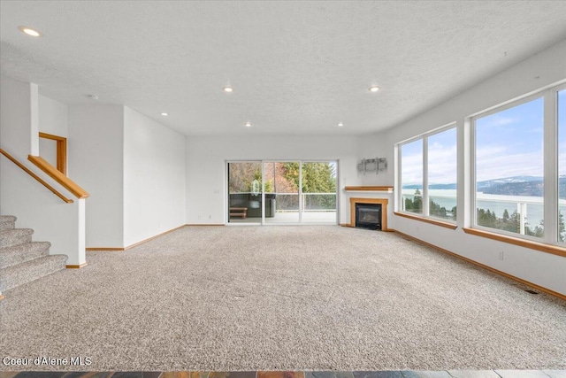 unfurnished living room with carpet floors, a textured ceiling, and a water view