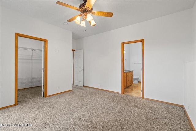 unfurnished bedroom with light carpet, ceiling fan, ensuite bath, a walk in closet, and a closet