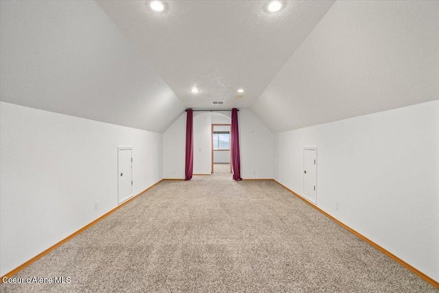 additional living space featuring vaulted ceiling, light colored carpet, and a textured ceiling