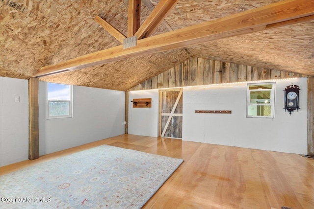 additional living space featuring wood-type flooring and lofted ceiling with beams