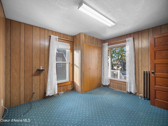 spare room featuring wooden walls, radiator heating unit, and a textured ceiling