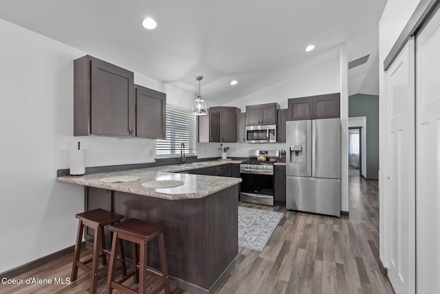 kitchen with vaulted ceiling, appliances with stainless steel finishes, pendant lighting, hardwood / wood-style flooring, and kitchen peninsula