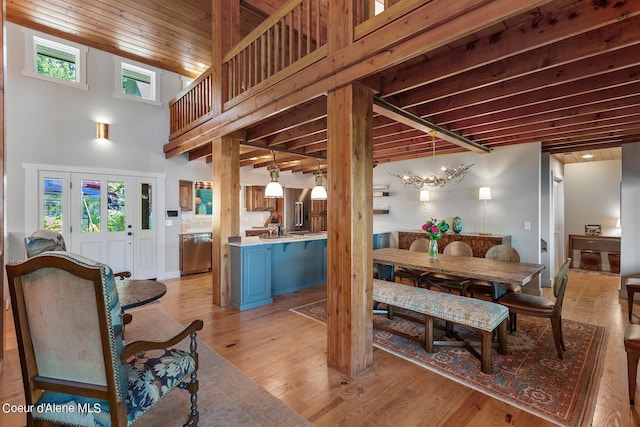 dining area featuring a towering ceiling, plenty of natural light, a notable chandelier, and light hardwood / wood-style floors