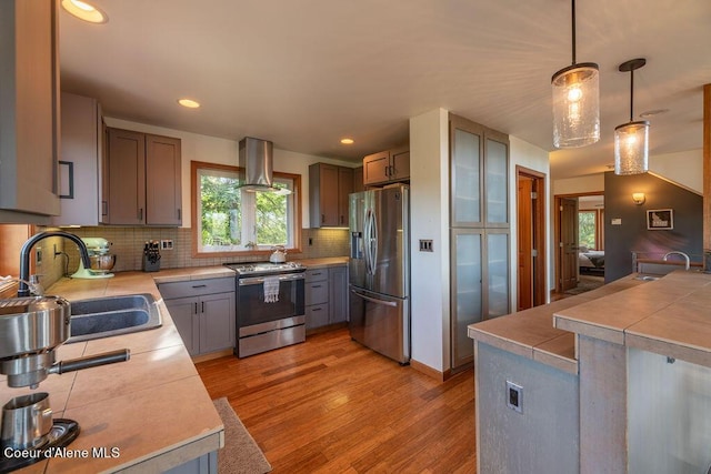 kitchen with backsplash, range hood, pendant lighting, sink, and appliances with stainless steel finishes