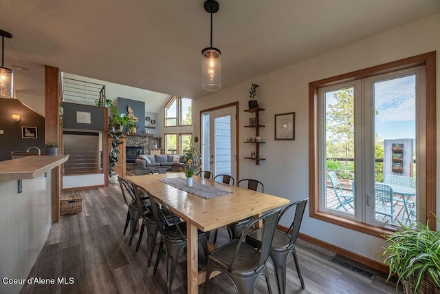 dining area with lofted ceiling, dark wood-type flooring, and a stone fireplace