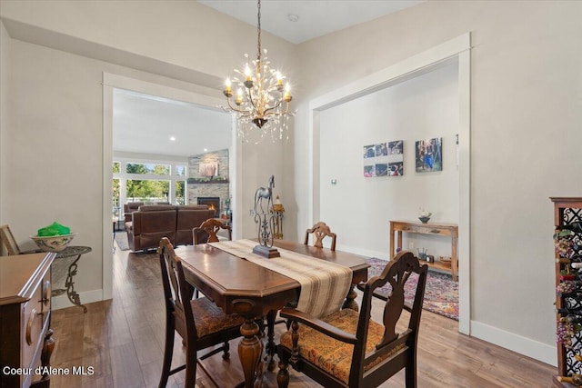 dining area with a chandelier, a fireplace, baseboards, and wood finished floors