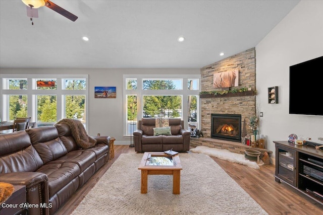 living area with lofted ceiling, a stone fireplace, wood finished floors, and recessed lighting